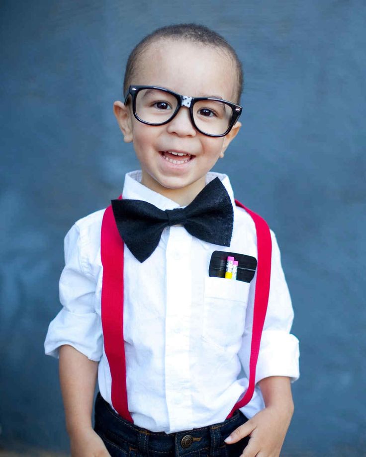 a young boy wearing glasses and a bow tie smiles at the camera while standing in front of a blue wall