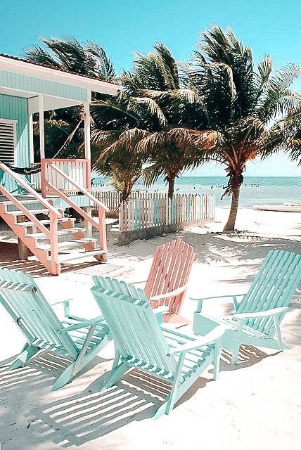 three lawn chairs sitting on the beach next to some palm trees and a blue house