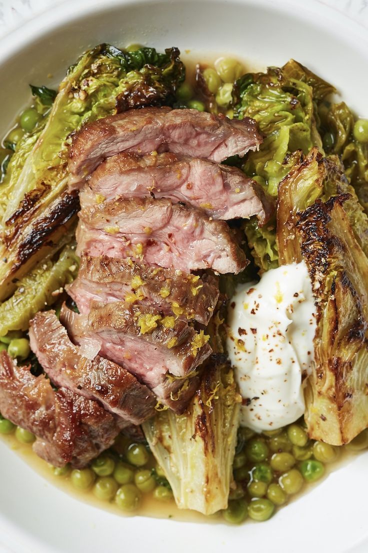 a white bowl filled with meat and vegetables on top of a table next to a fork