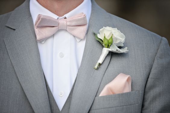 a man in a gray suit with a pink bow tie and boutonniere