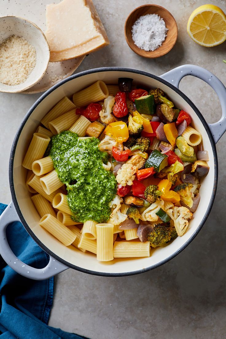 a pot filled with pasta and vegetables on top of a table next to sliced lemons