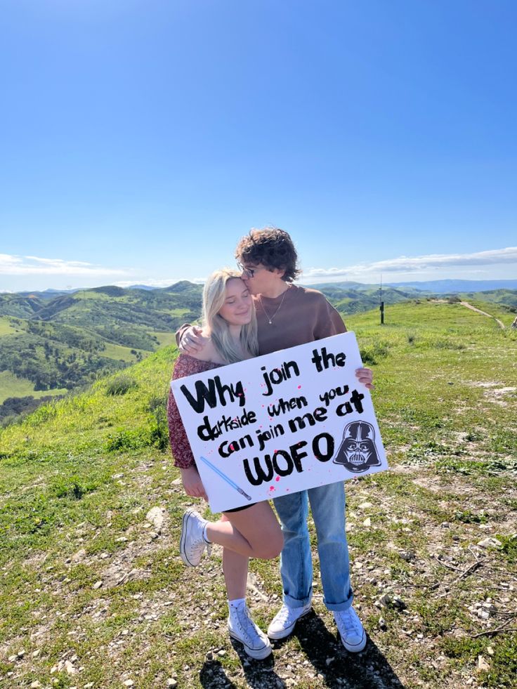 a man and woman standing on top of a hill holding a sign that says why join the