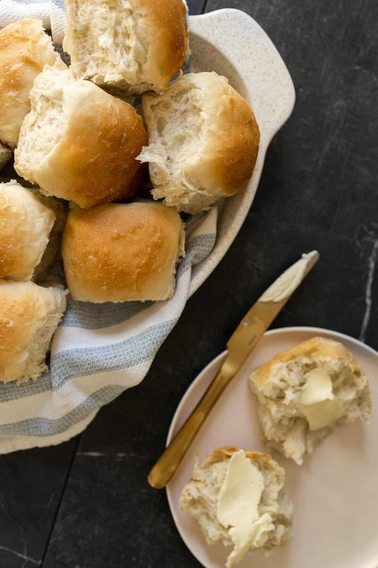 a plate with rolls and butter on it next to a bowl of buttery biscuits