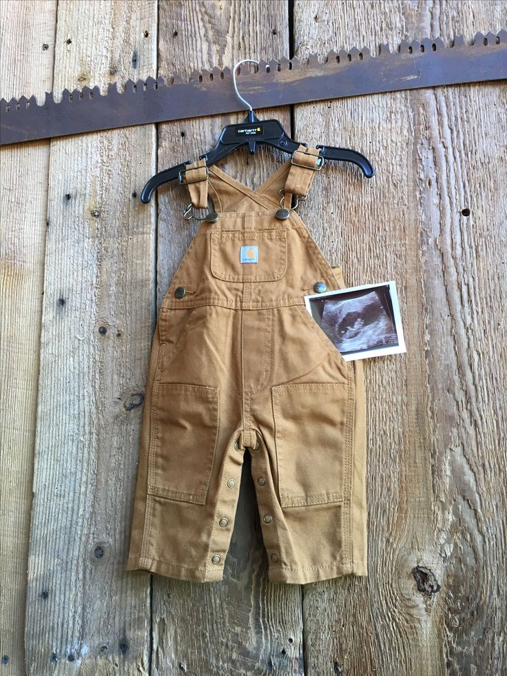 a pair of brown overalls hanging on a wooden wall next to a saw blade