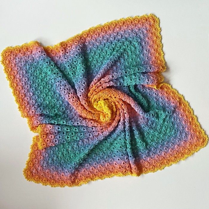 a multicolored crocheted square on top of a white surface with a yellow center