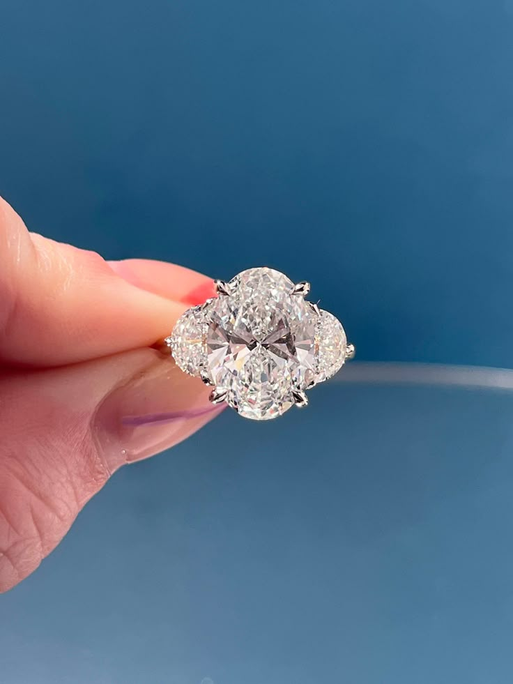 a woman's hand holding a three stone diamond ring in front of a blue background