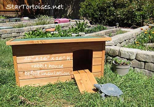 a small wooden dog house in the middle of some grass and plants with writing on it