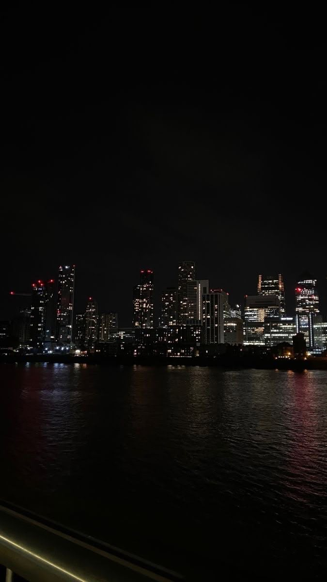 the city skyline is lit up at night with lights reflecting on the water and buildings in the background