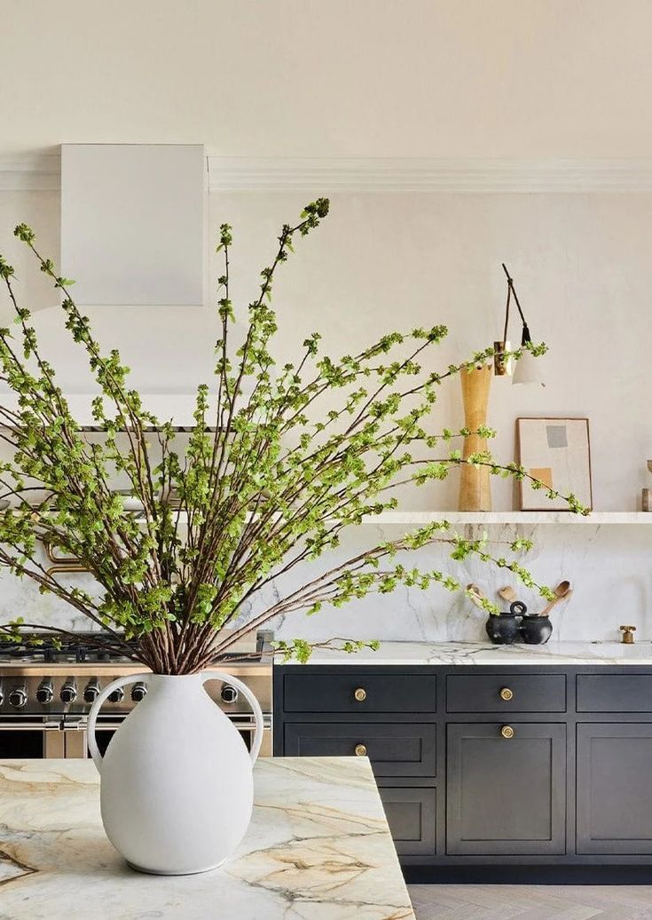 a white vase filled with green plants on top of a kitchen counter next to an oven