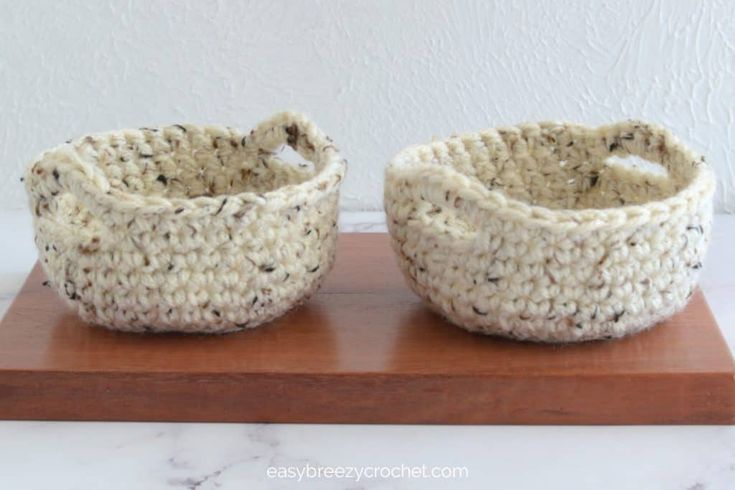 two crocheted baskets sitting on top of a wooden board