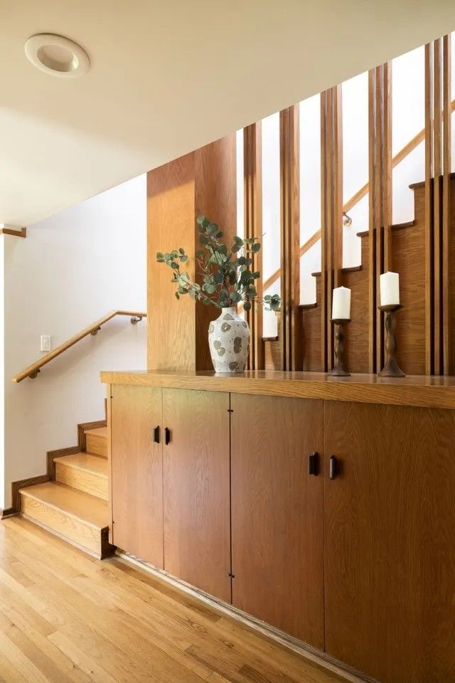 a room with wood floors and wooden cabinets next to a stair case in front of a window