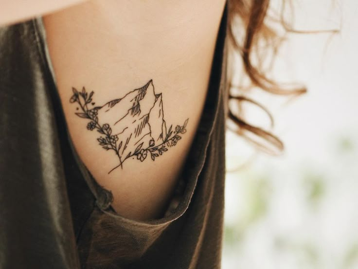 a woman with a tattoo on her neck that has mountains and flowers in the middle