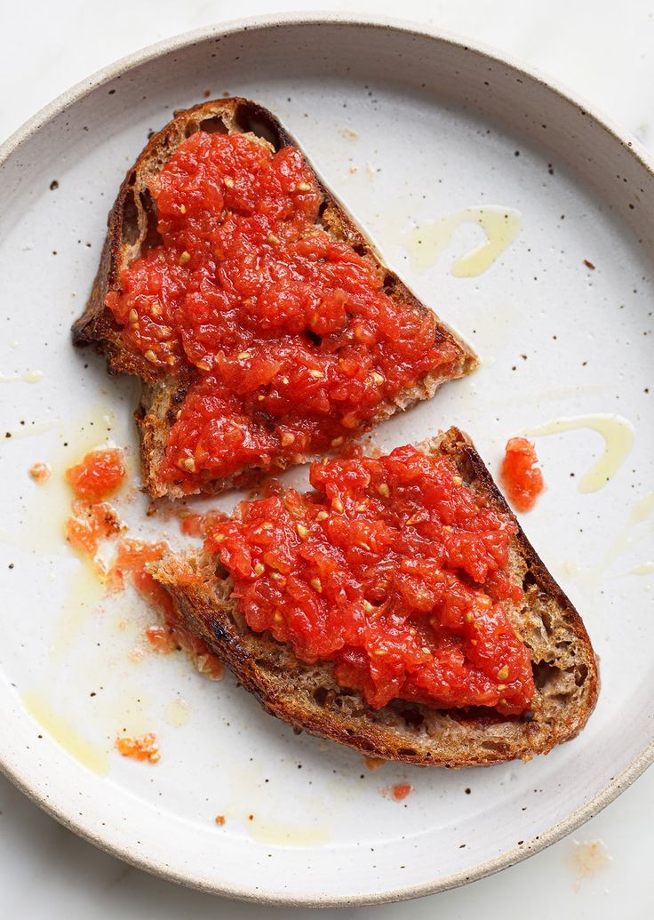 two pieces of bread with marinara sauce on them sitting on a white plate, ready to be eaten