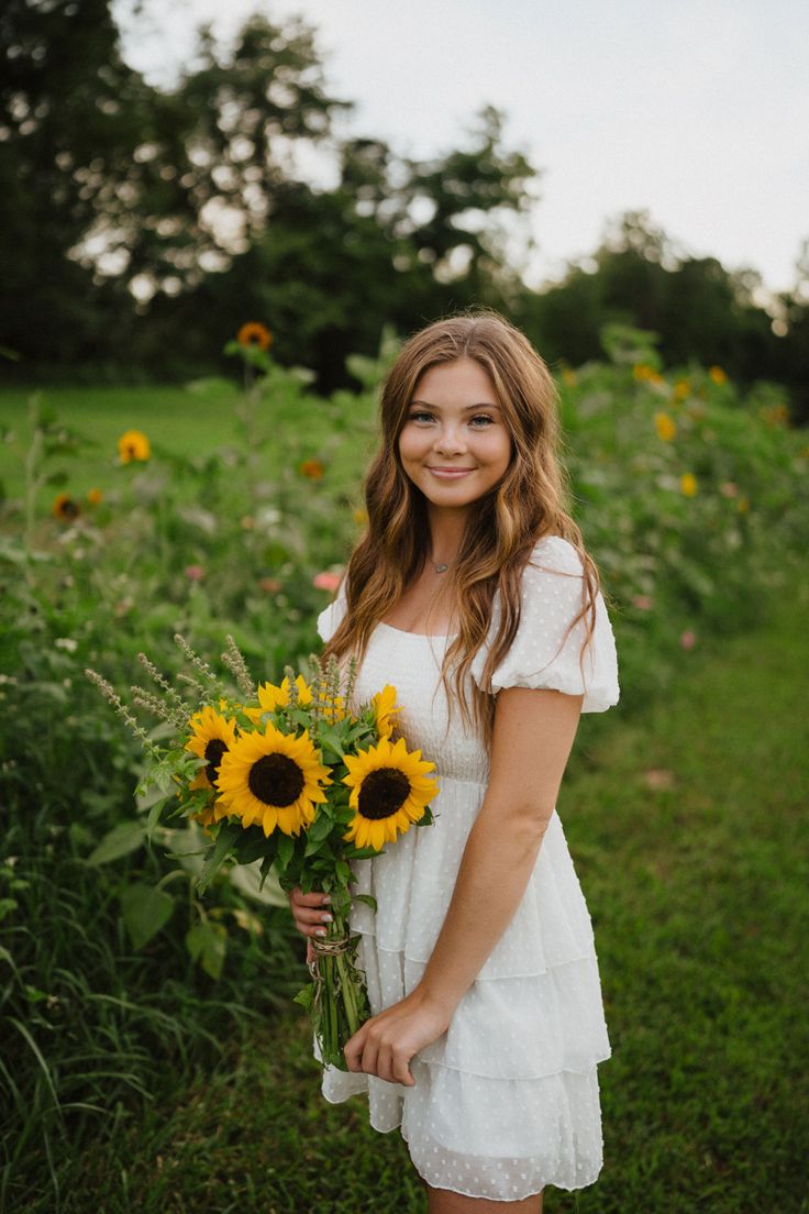 a woman in a white dress is holding sunflowers and smiling at the camera