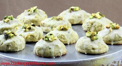 a tin filled with cookies covered in white frosting and pistachio toppings