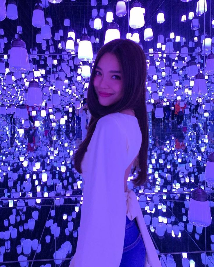 a woman standing in front of a wall with many lights hanging from it's sides