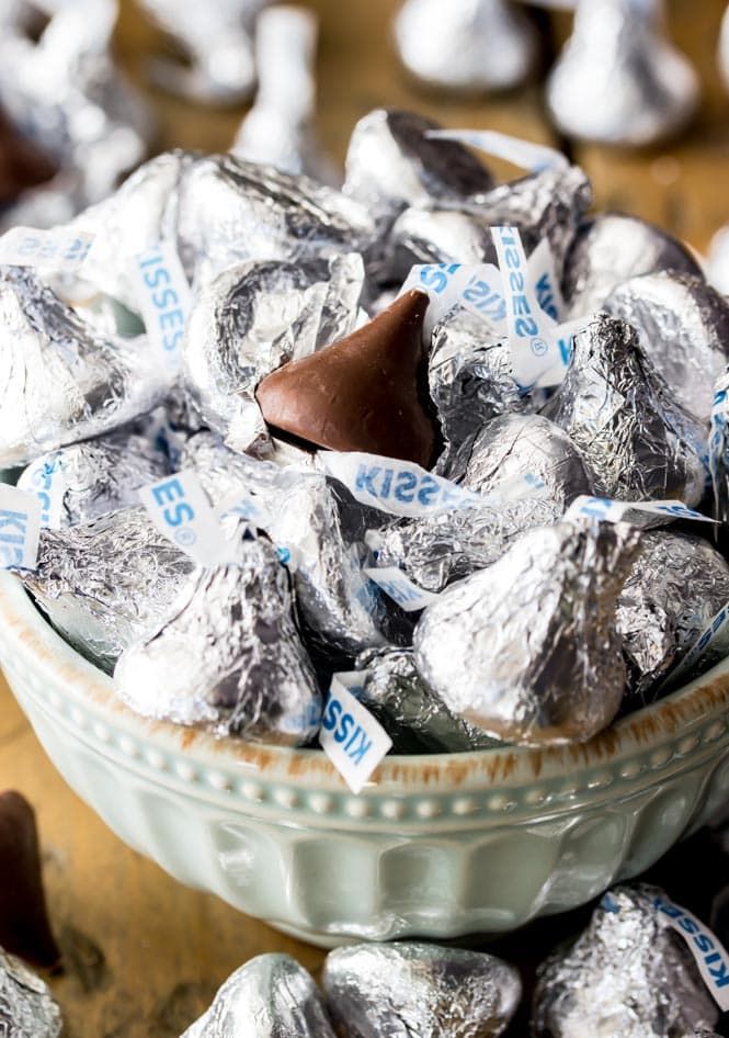 a bowl filled with silver foiled chocolates on top of a wooden table next to other candies