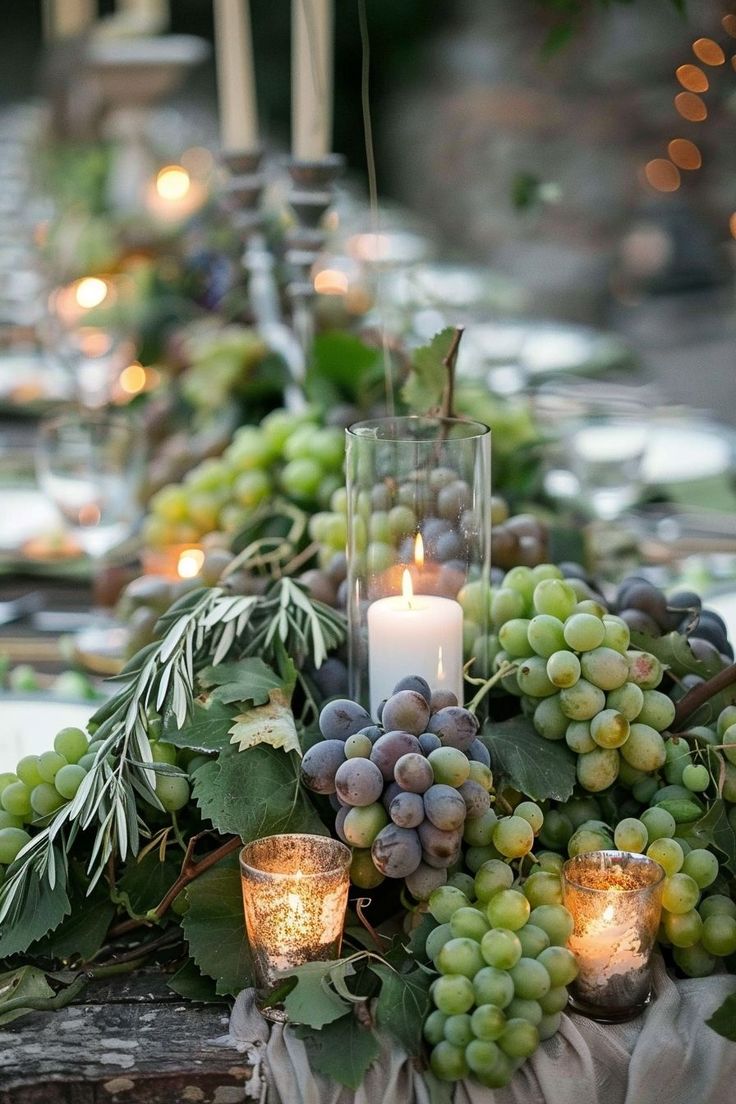 the table is set with candles, grapes and greenery