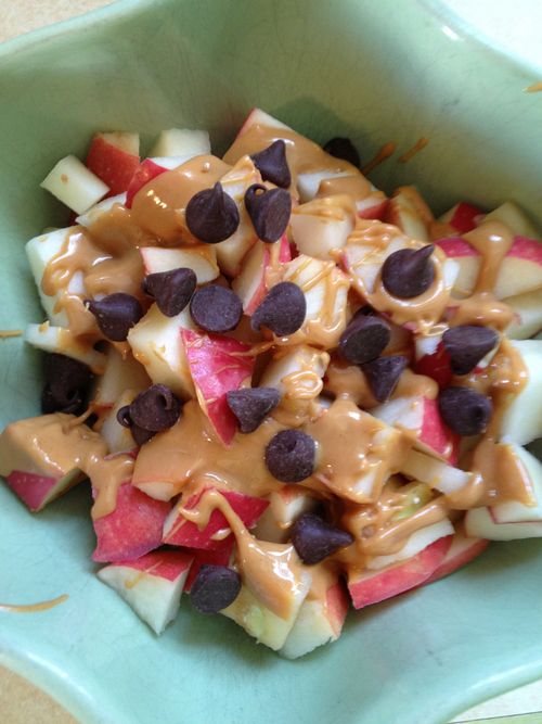 an apple salad with chocolate chips and caramel sauce in a green bowl on a table