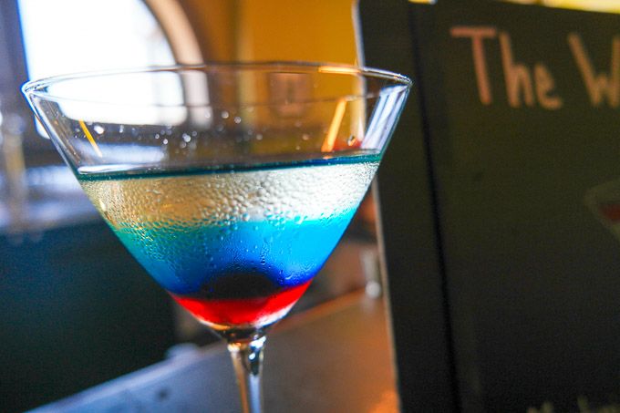 a blue and red drink sitting on top of a table next to a menu board