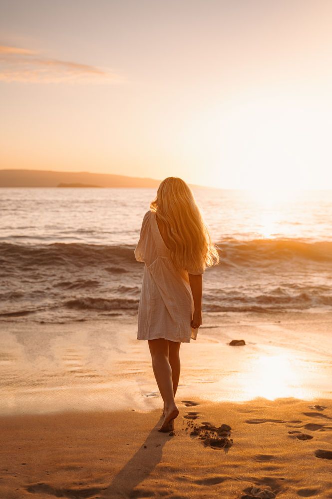 a woman walking on the beach at sunset with her hair blowing in the wind,