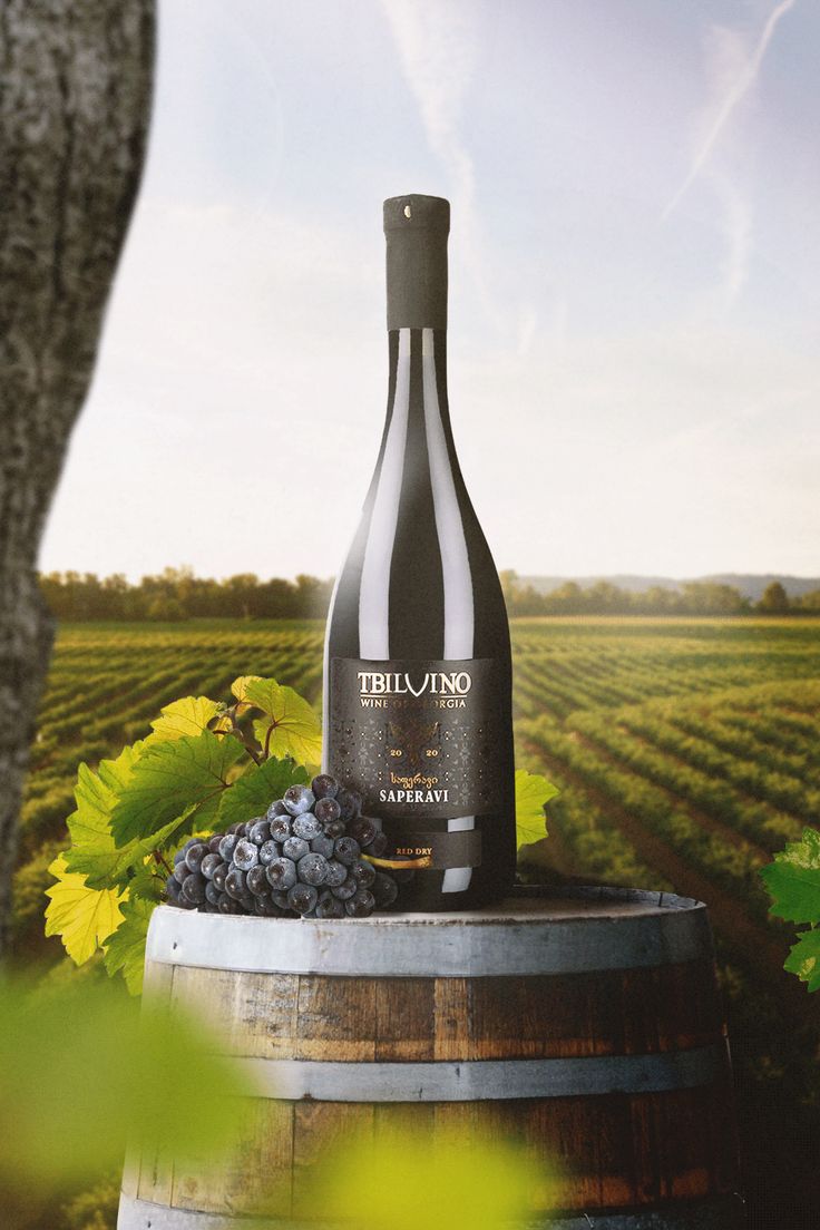 a bottle of wine sitting on top of a barrel next to some grapes in a vineyard