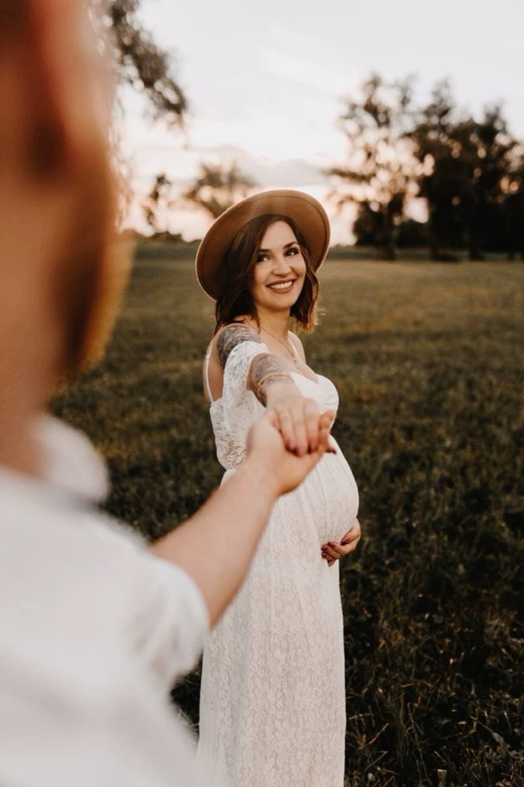 a pregnant woman in a white dress and hat holding the hand of a man wearing a brown hat