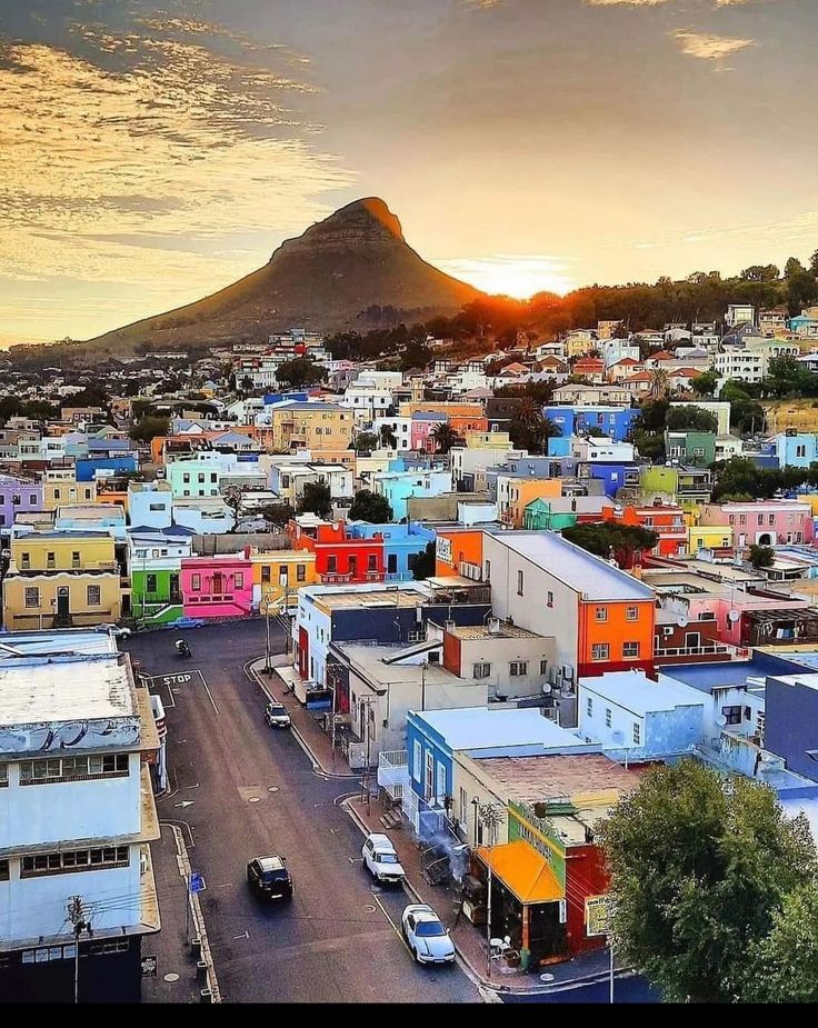 an aerial view of a city with colorful buildings and mountains in the background at sunset