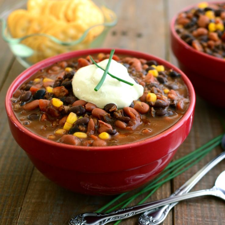 two red bowls filled with chili, beans and corn on top of a wooden table