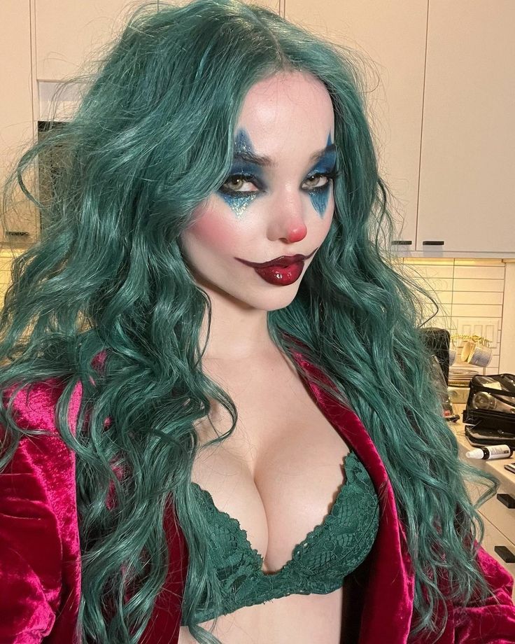 a woman with green hair and makeup is dressed in a red jacket, black bra and blue eyeshadow