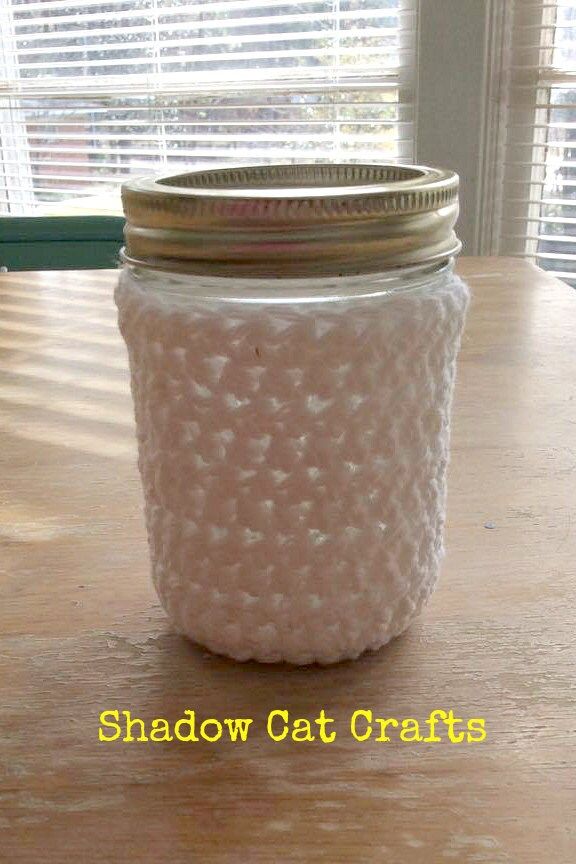 a mason jar filled with white crochet sits on a table next to a window