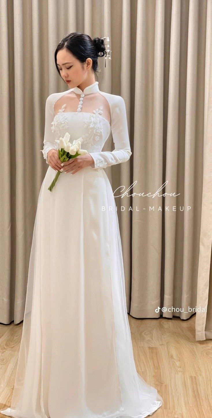 a woman in a white wedding dress holding a flower and standing next to a curtain