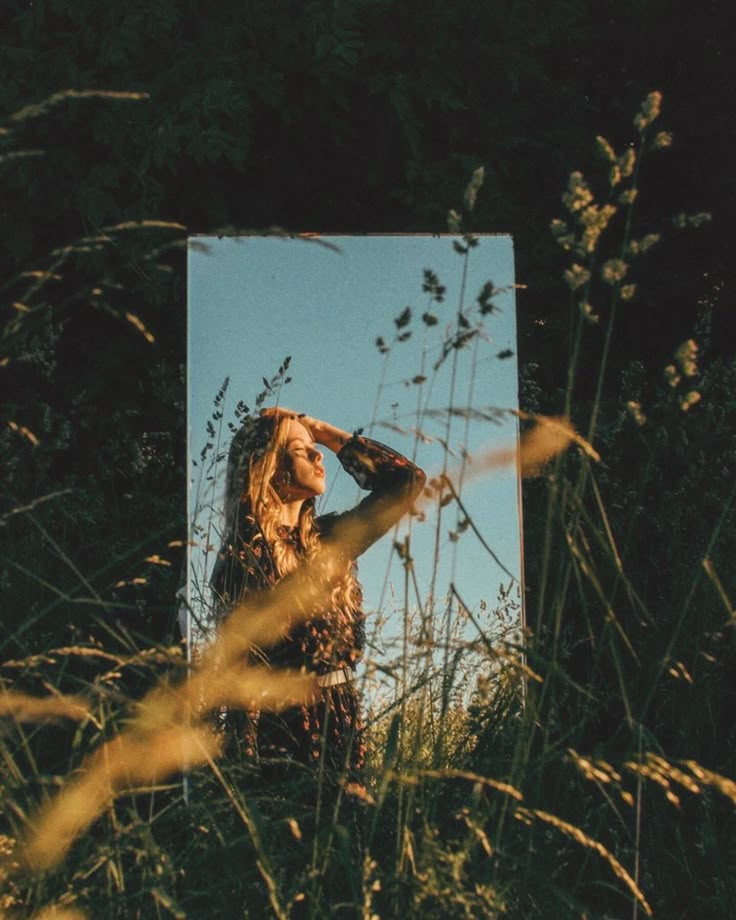 a woman standing in tall grass with her hand on her head looking at the sky