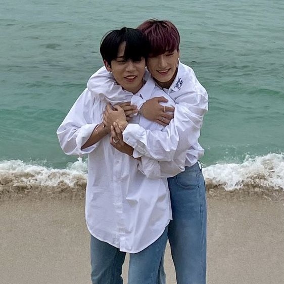 two people hugging on the beach with water in the background and one person standing behind them