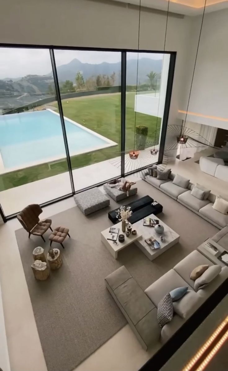 a living room with couches and tables in front of large windows overlooking a swimming pool