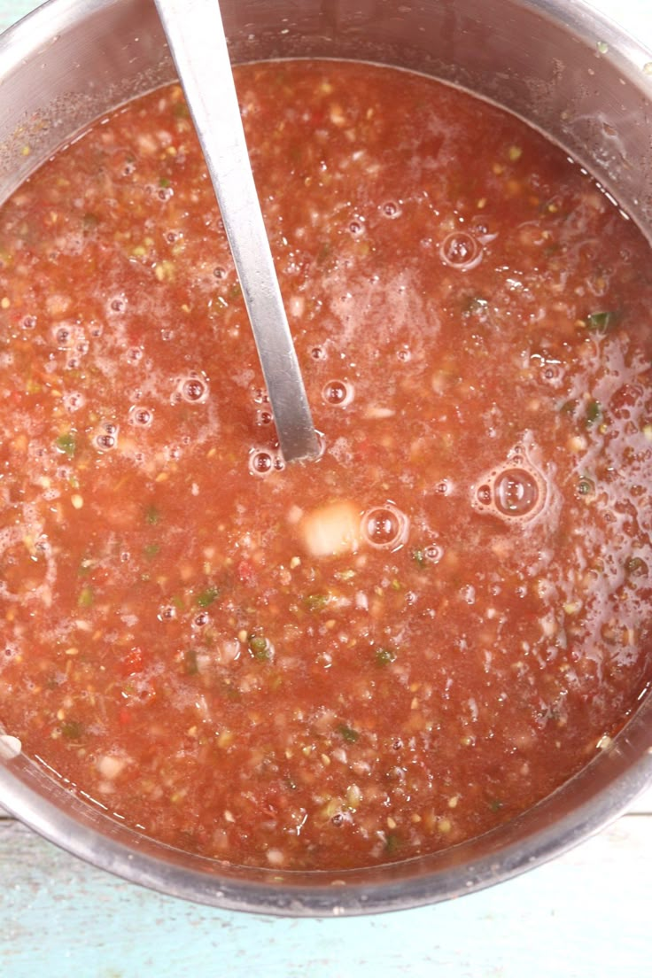 a pot full of soup with a ladle in the bowl next to it on a blue table