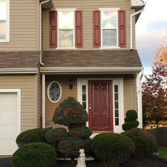 a house with red shutters and trees in front