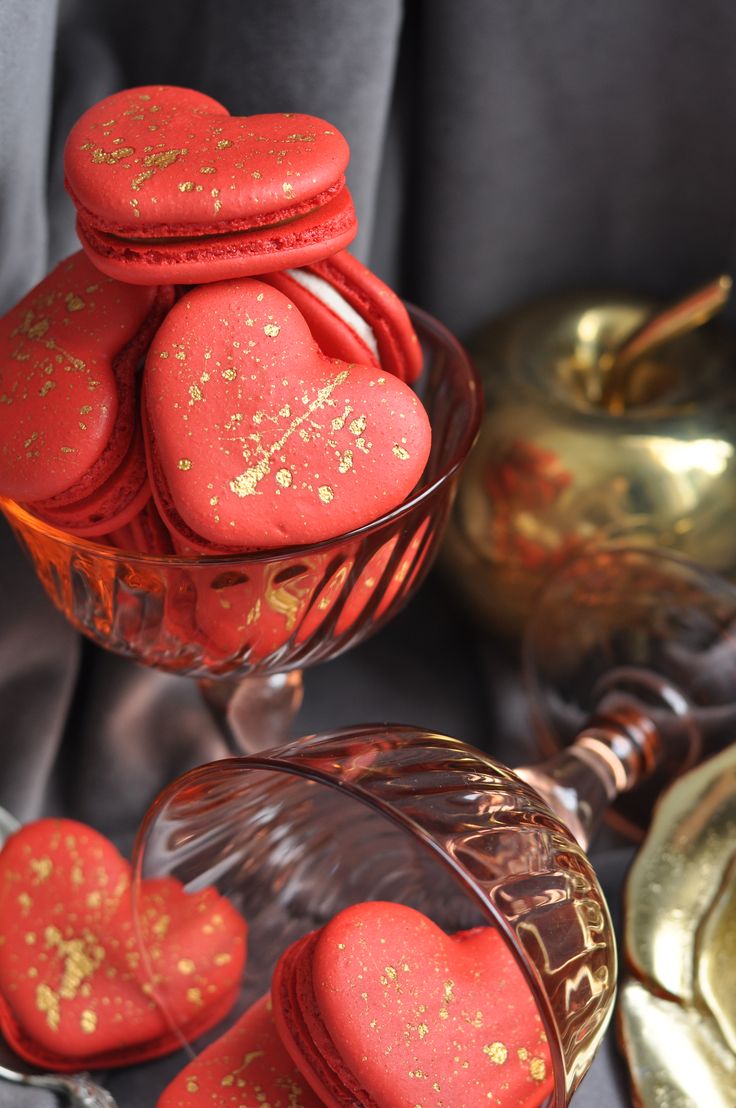 red heart shaped cookies sitting in a glass bowl next to other gold and silver items