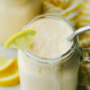 two mason jars filled with smoothie and garnished with lemon wedges on a table