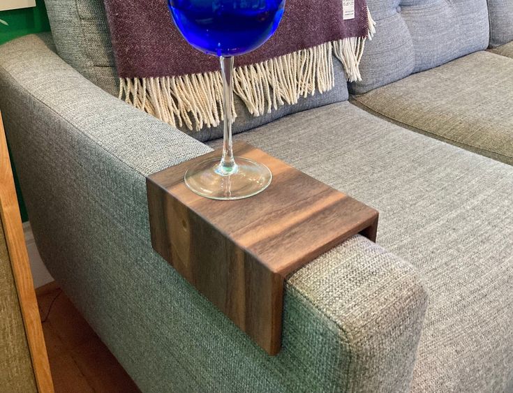 a blue wine glass sitting on top of a wooden table next to a gray couch