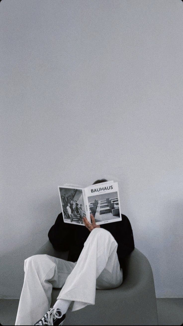 a man sitting in a chair reading a newspaper while wearing white pants and black shirt