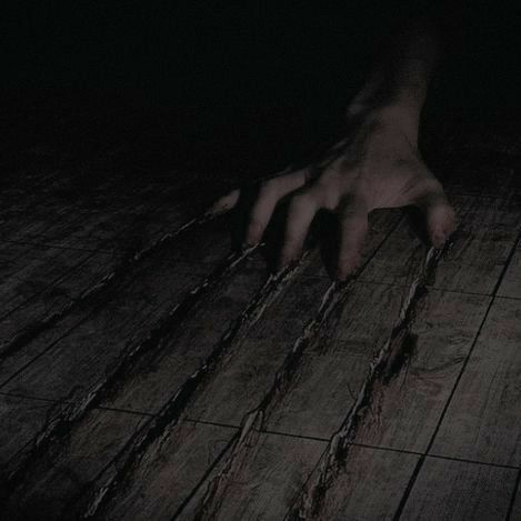 a creepy hand reaching for something in the dark with its claws spread out, on a wooden floor