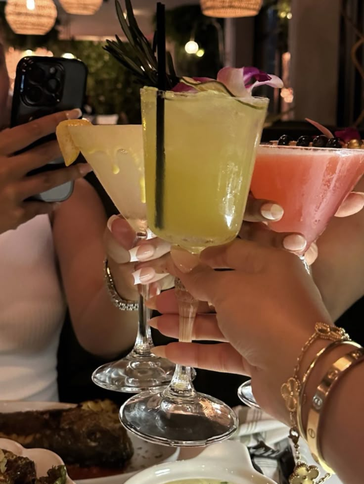 people holding up drinks at a table with food and drink glasses on it in front of them