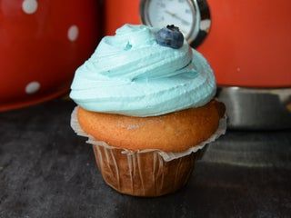 a cupcake with blue frosting on top next to an orange crockpot