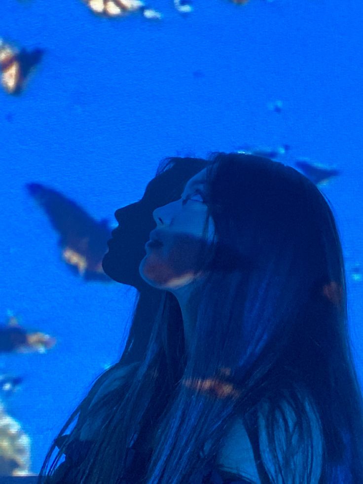 a woman with long hair standing in front of a blue background and looking up at birds