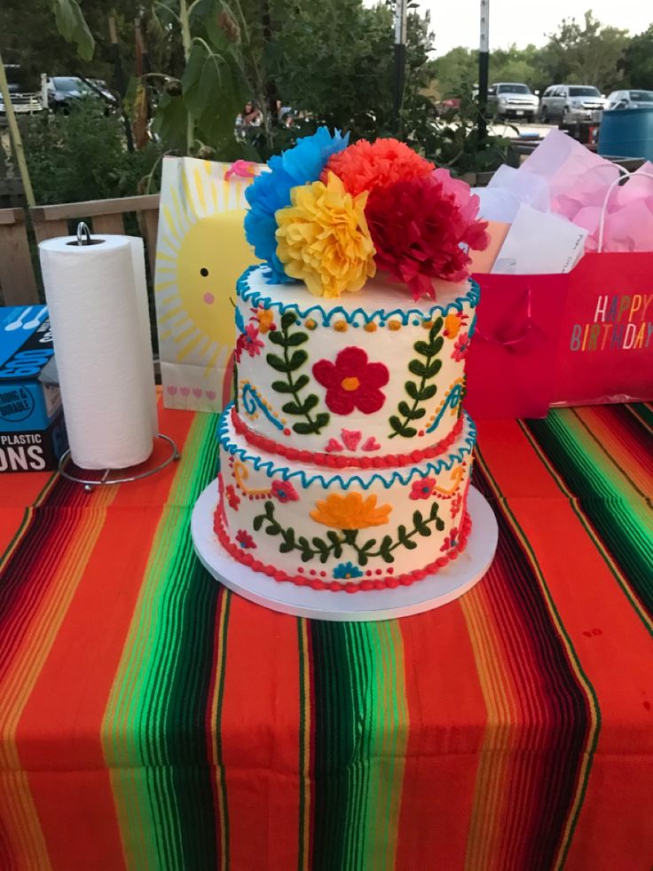 a multi - tiered cake with colorful flowers on top sits on a striped tablecloth