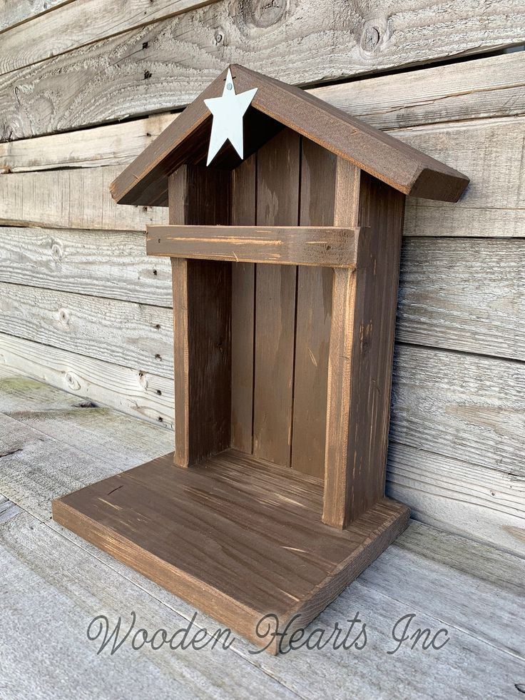 a wooden birdhouse with a white star on the top and bottom shelf, sitting against a wood wall