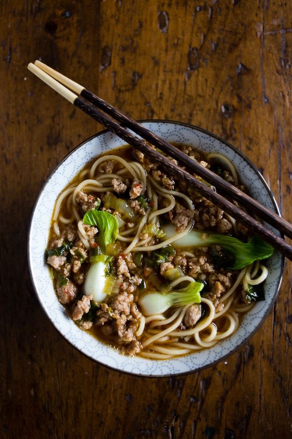 a bowl filled with noodles, meat and vegetables next to chopsticks on a wooden table