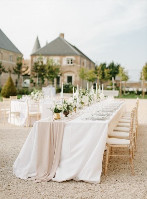 a long table is set with white flowers and candles for an outdoor wedding reception in front of a large house