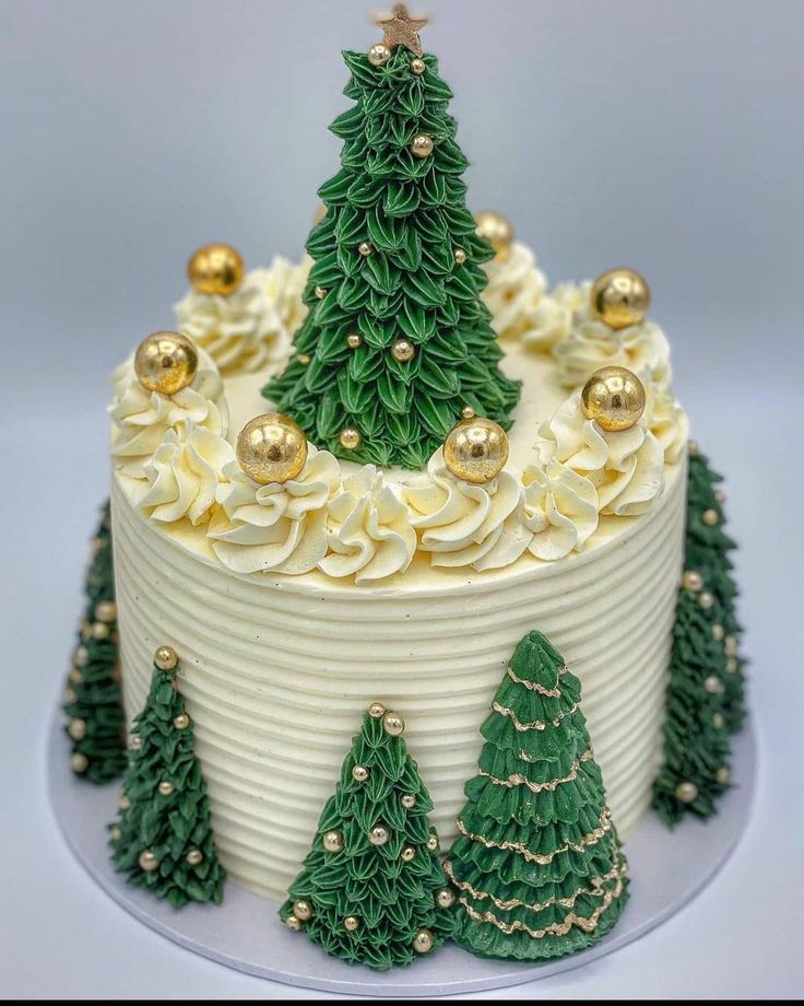 a christmas cake with white frosting and green trees on top, decorated with gold ornaments